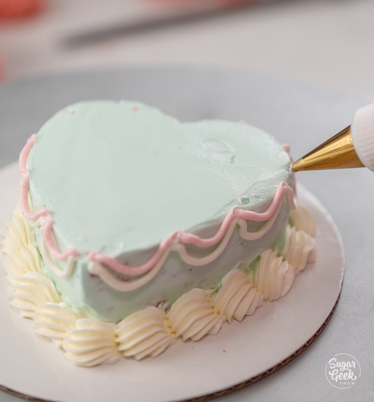 piping bag making a design on the side of a heart cake