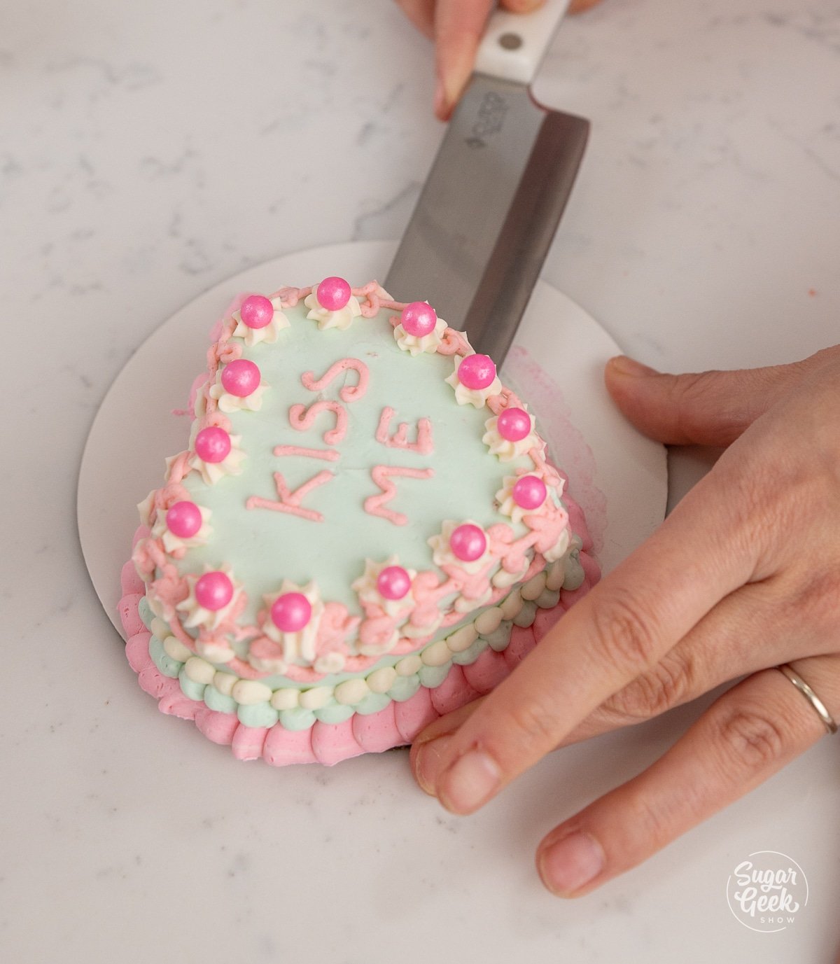 hand removing a heart cake from a cake board with a knife