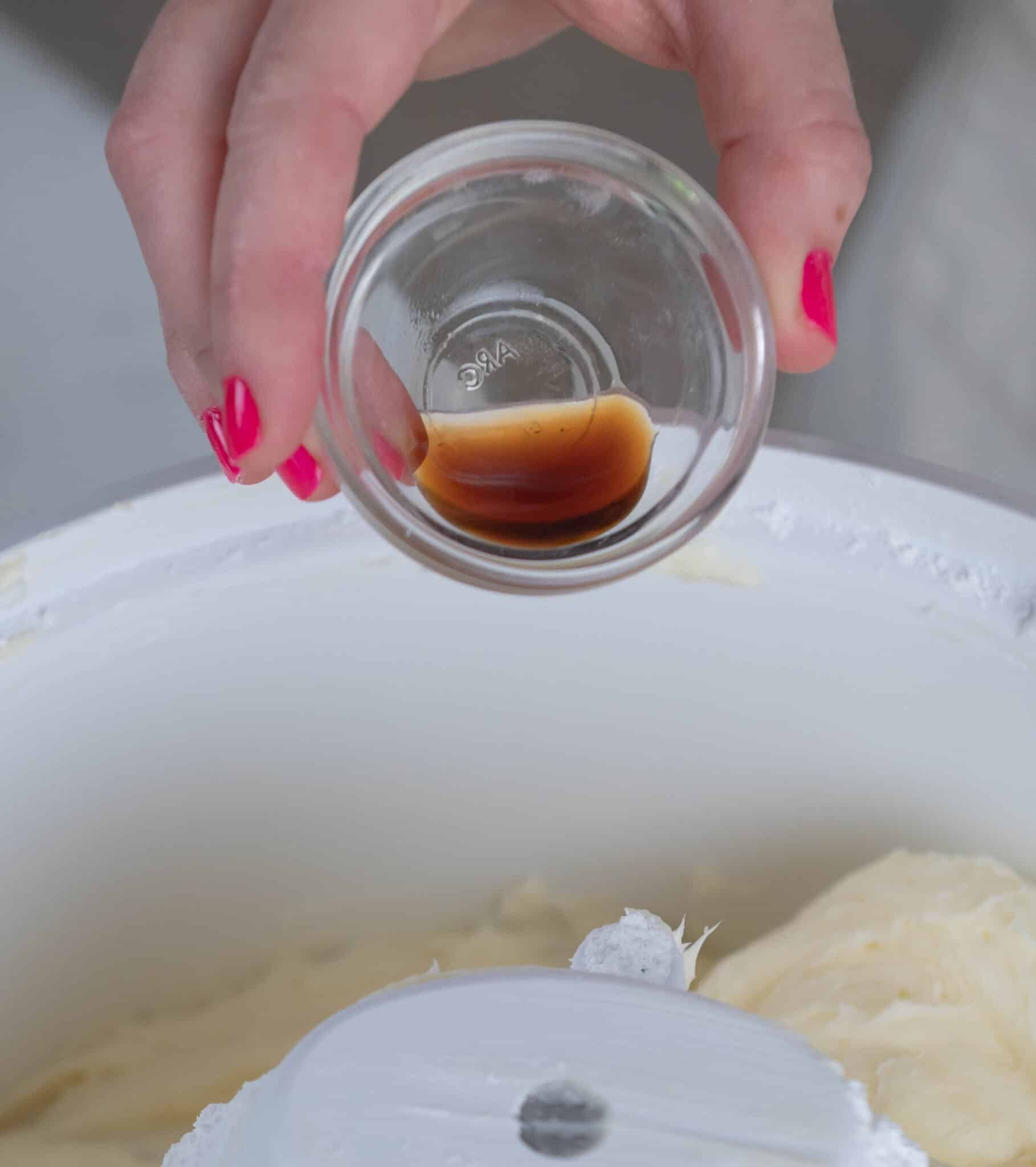 hand adding a bowl of vanilla into a stand mixer bowl