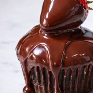 close up of a ganache covered strawberry on a chocolate cupcake