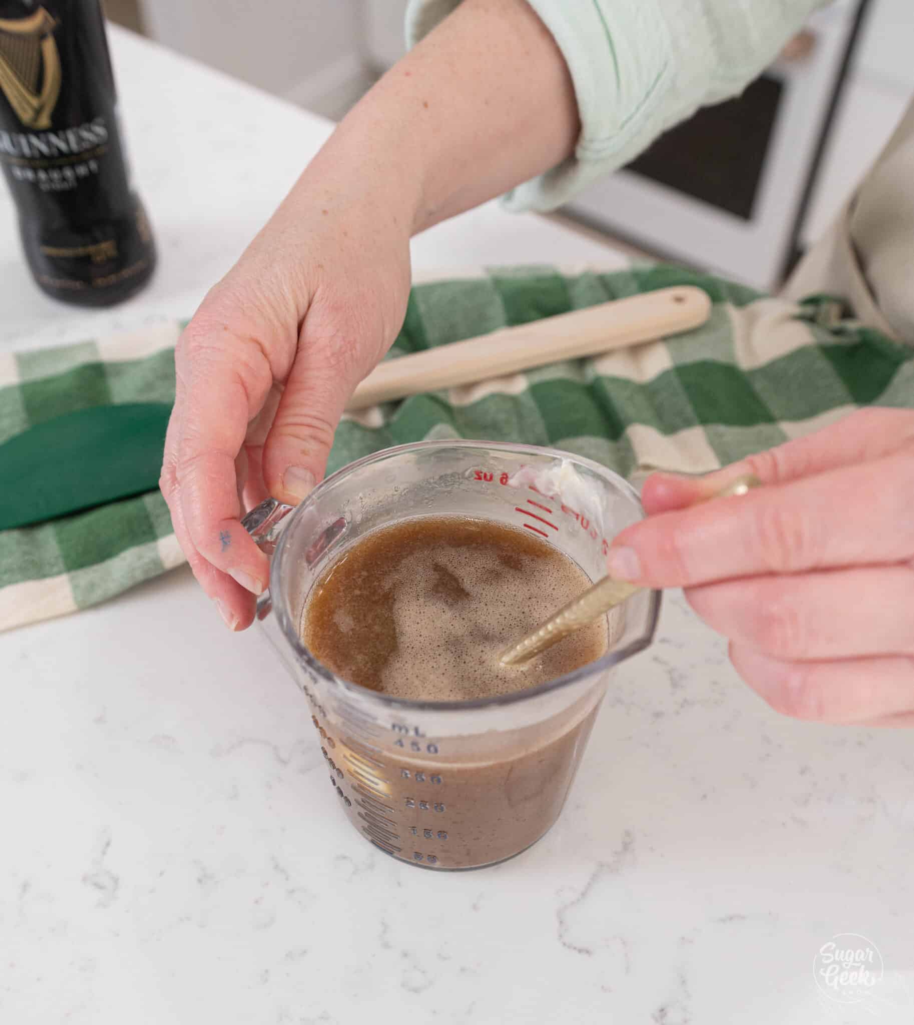 hands stirring melted butter and guinness with a spoon in a tall measuring cup