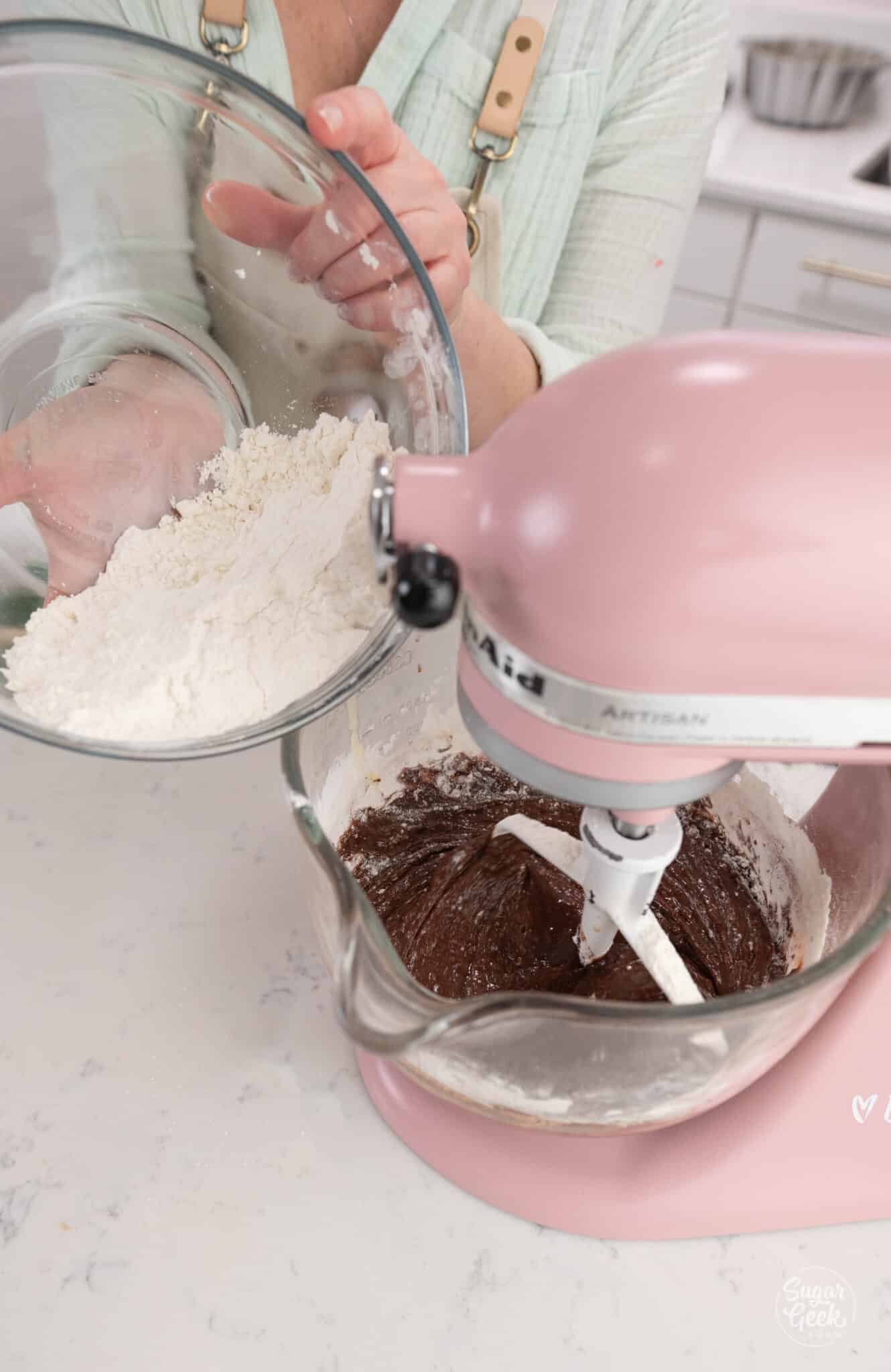 hands adding a bowl of dry ingredients to a stand mixer bowl