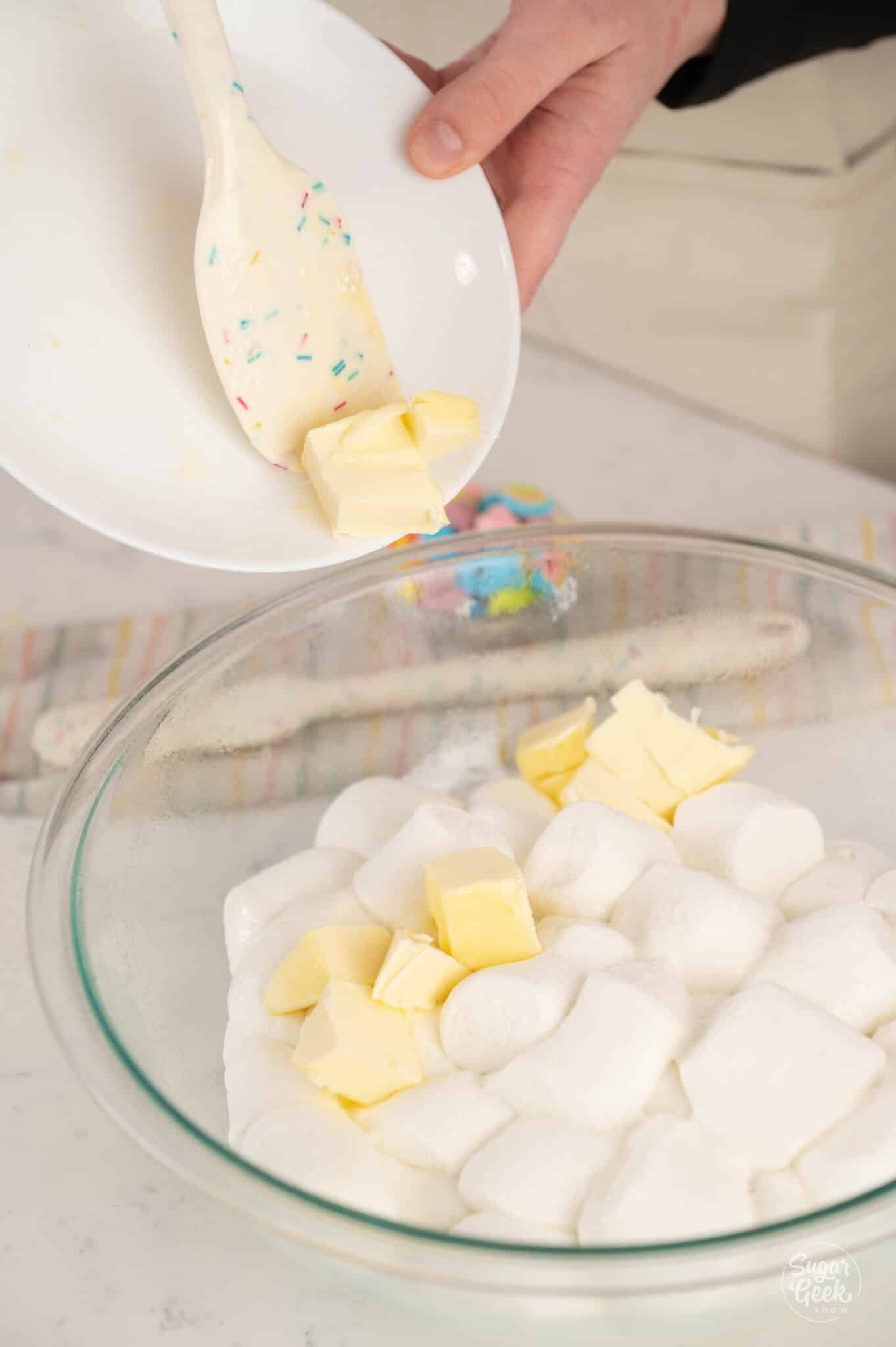 hands adding butter from a plate into a bowl of marshmallows