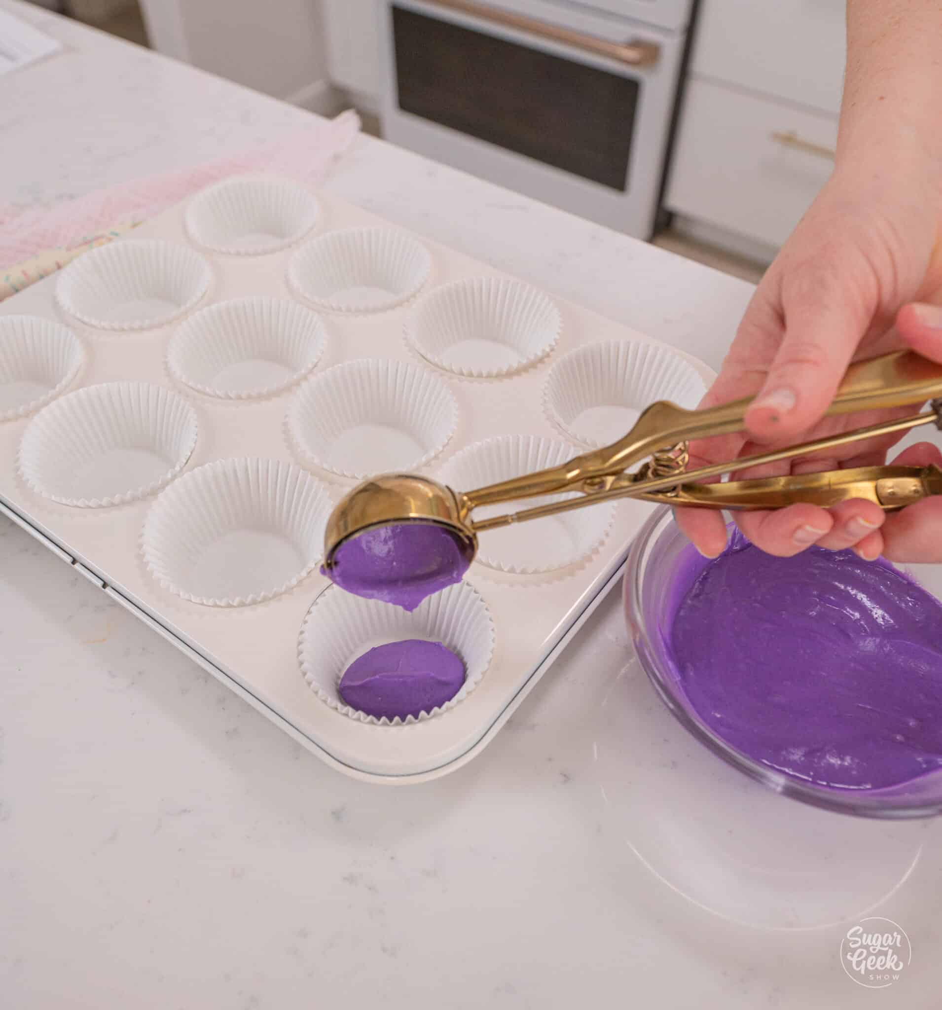 dividing purple batter into cupcake trays with a cookie scoop