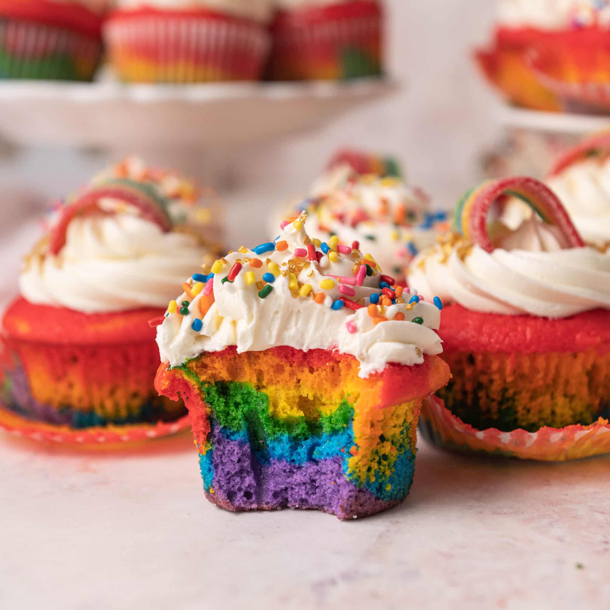 rainbow cupcake with a bite taken out of it next to other rainbow cupccakes