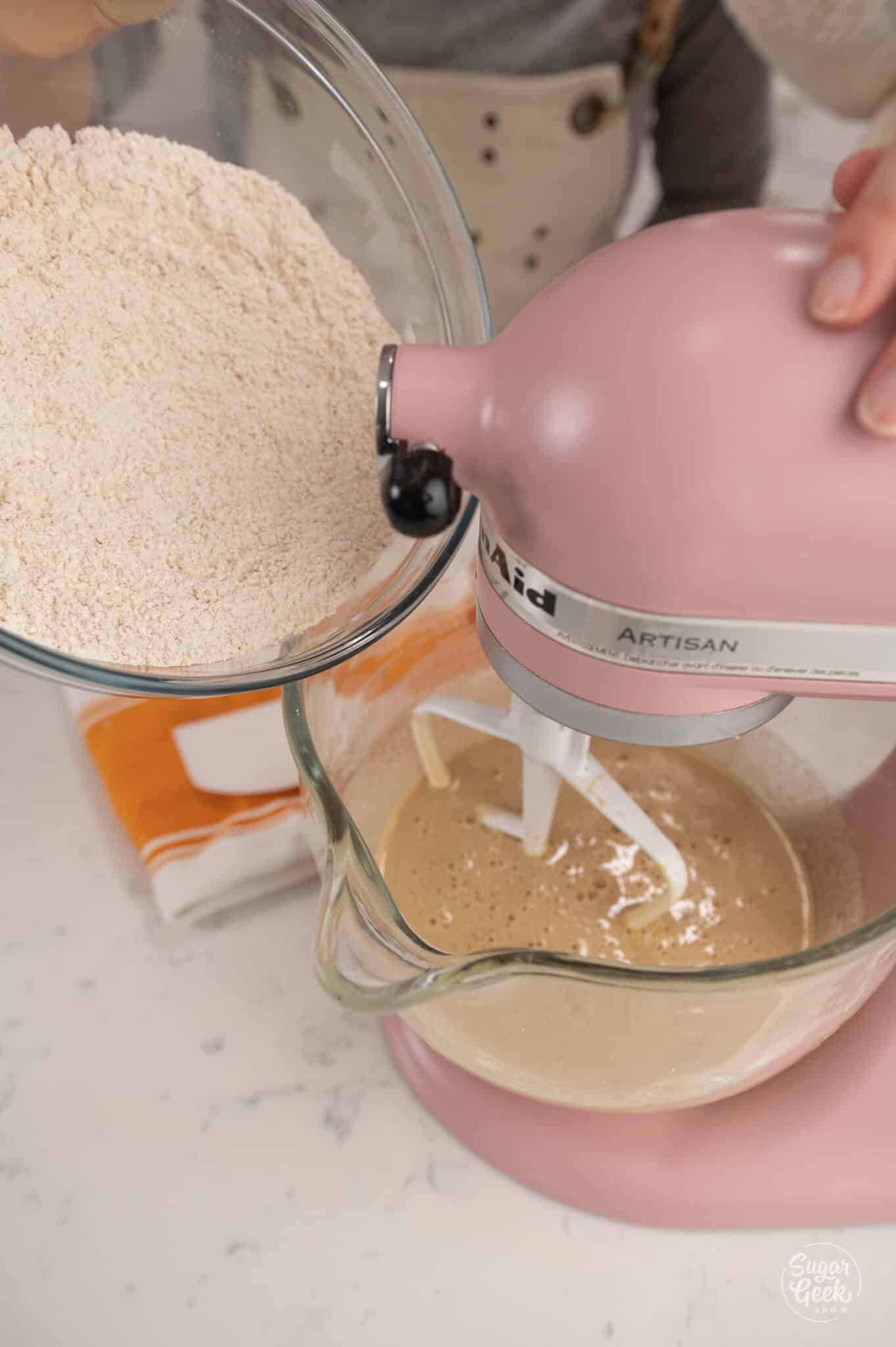 Hand adding a bowl of flour to a stand mixer bowl