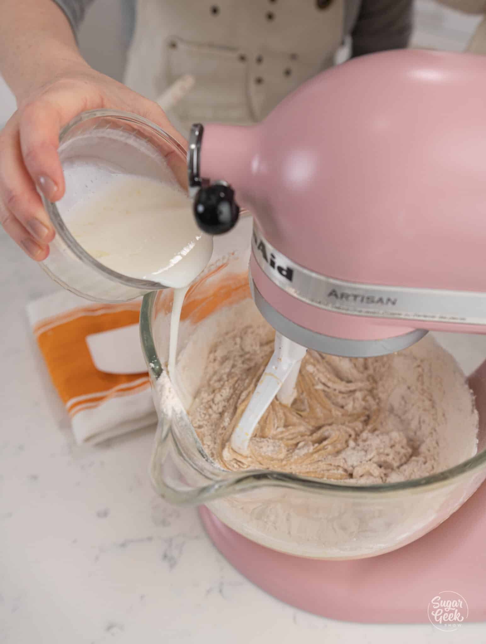 Hand adding buttermilk to a stand mixer bowl of batter