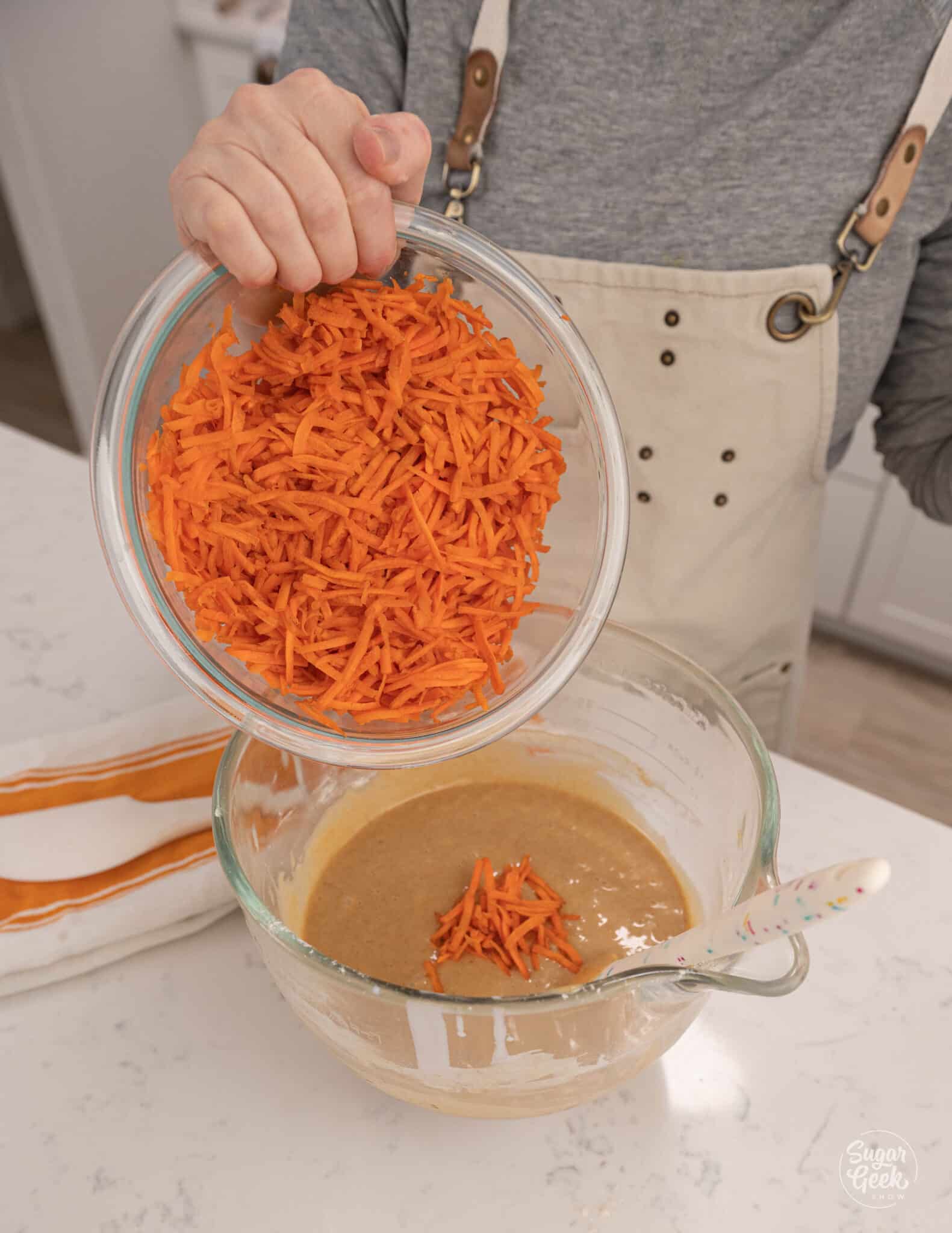 Hand adding a bowl of carrots to batter