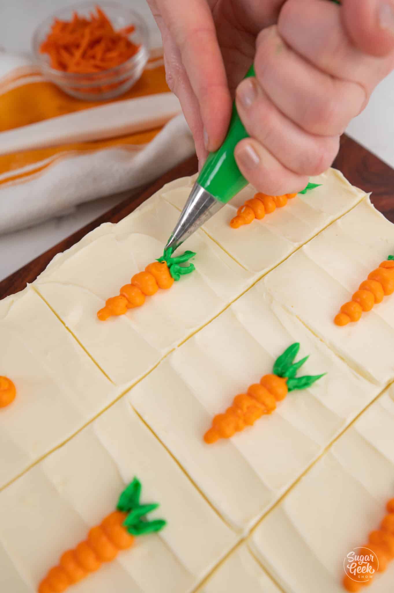 piping green frosting leaves next to a frosting carrot