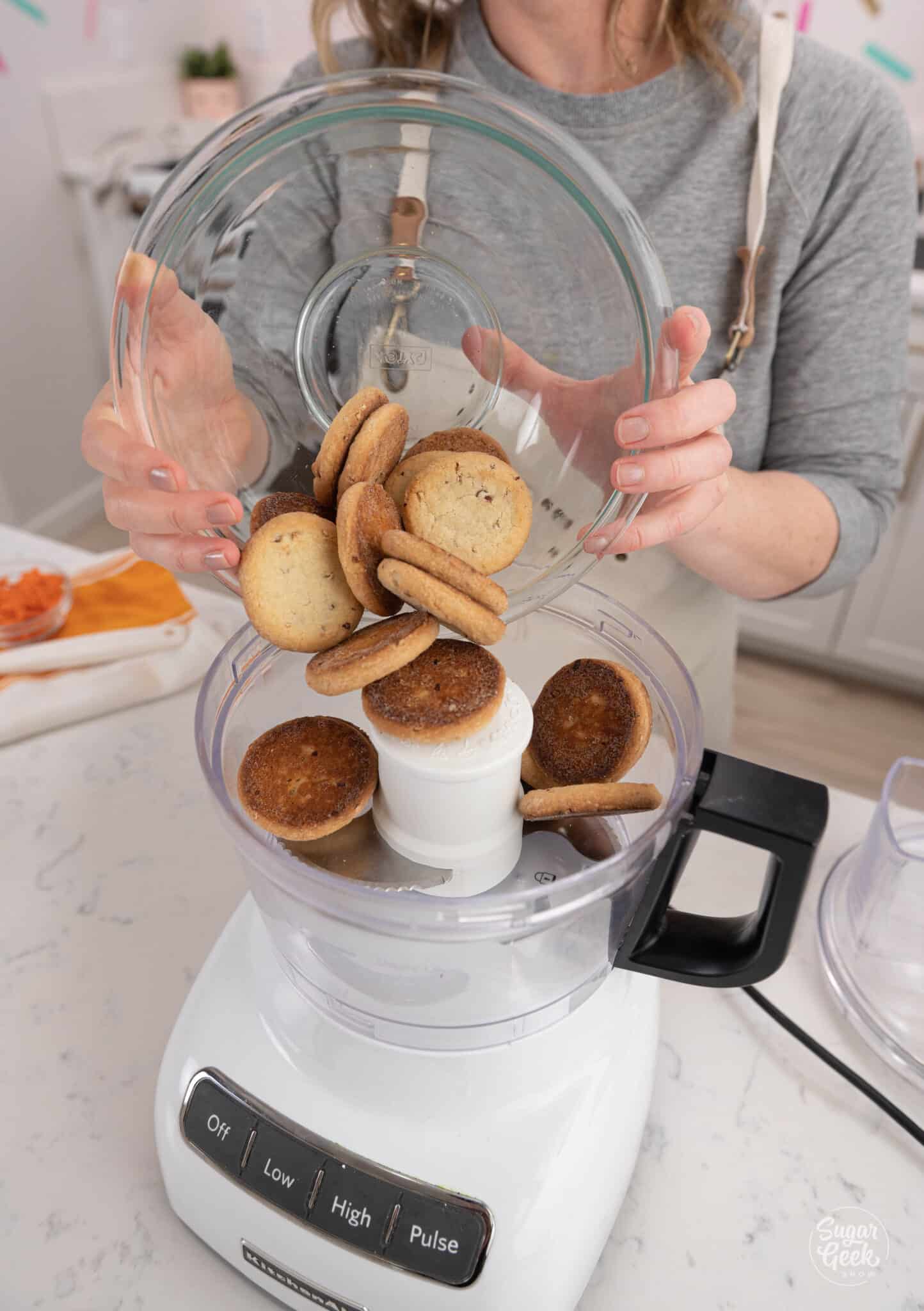 Hands adding a bowl of cookies into a food processor