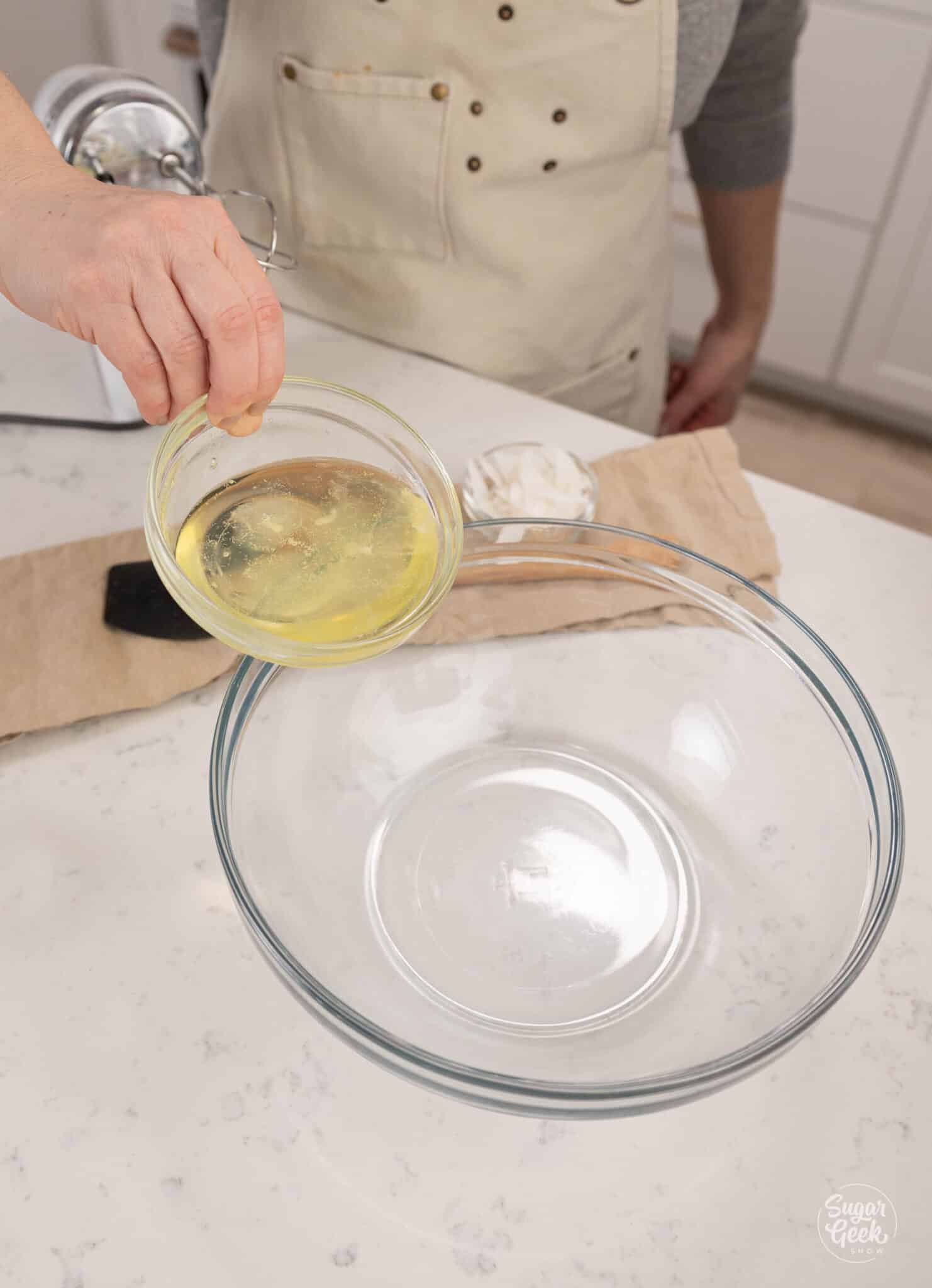 hand adding a bowl of egg whites to a clear bowl