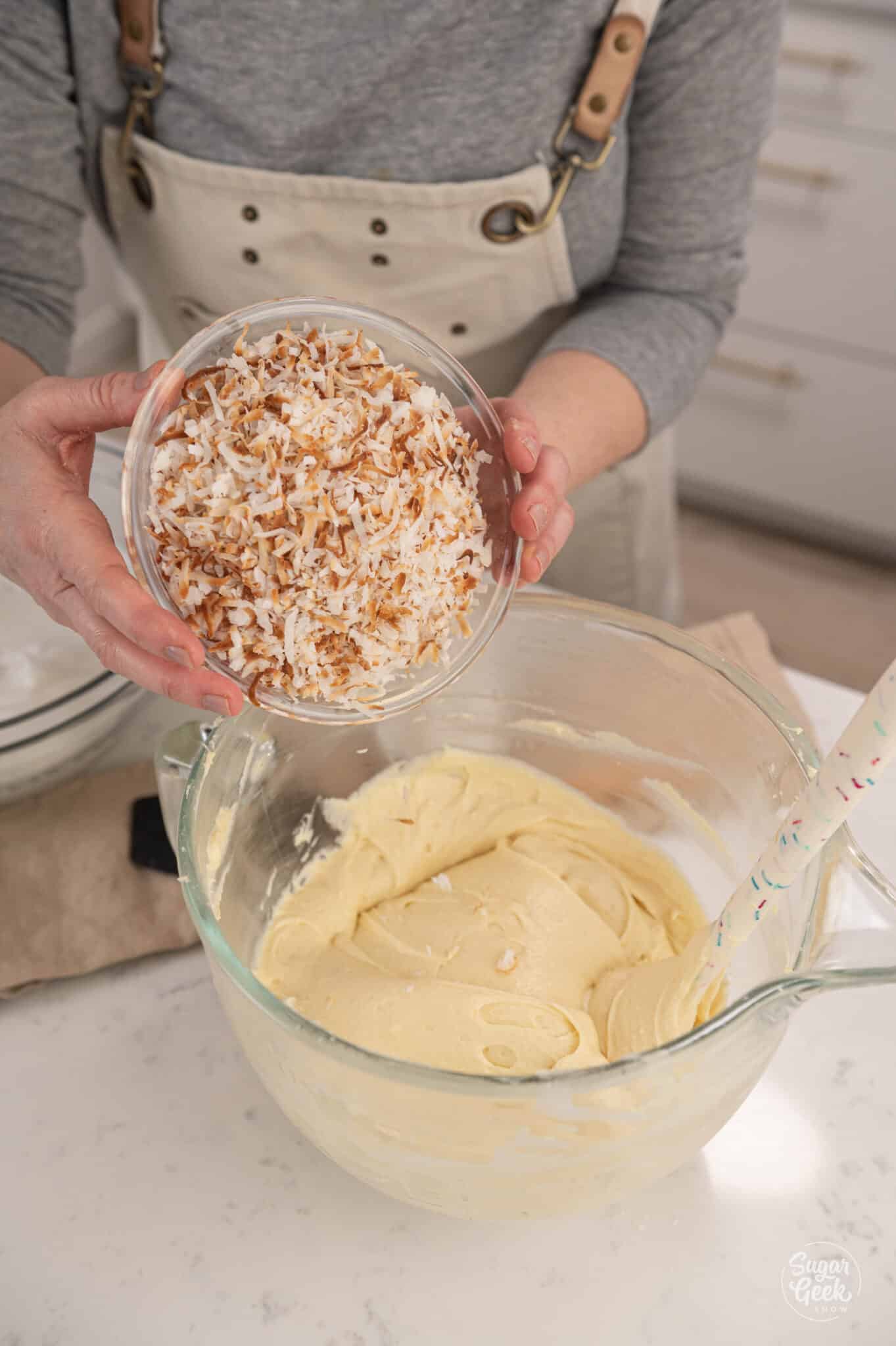 hands adding a bowl of toasted coconut to cake batter