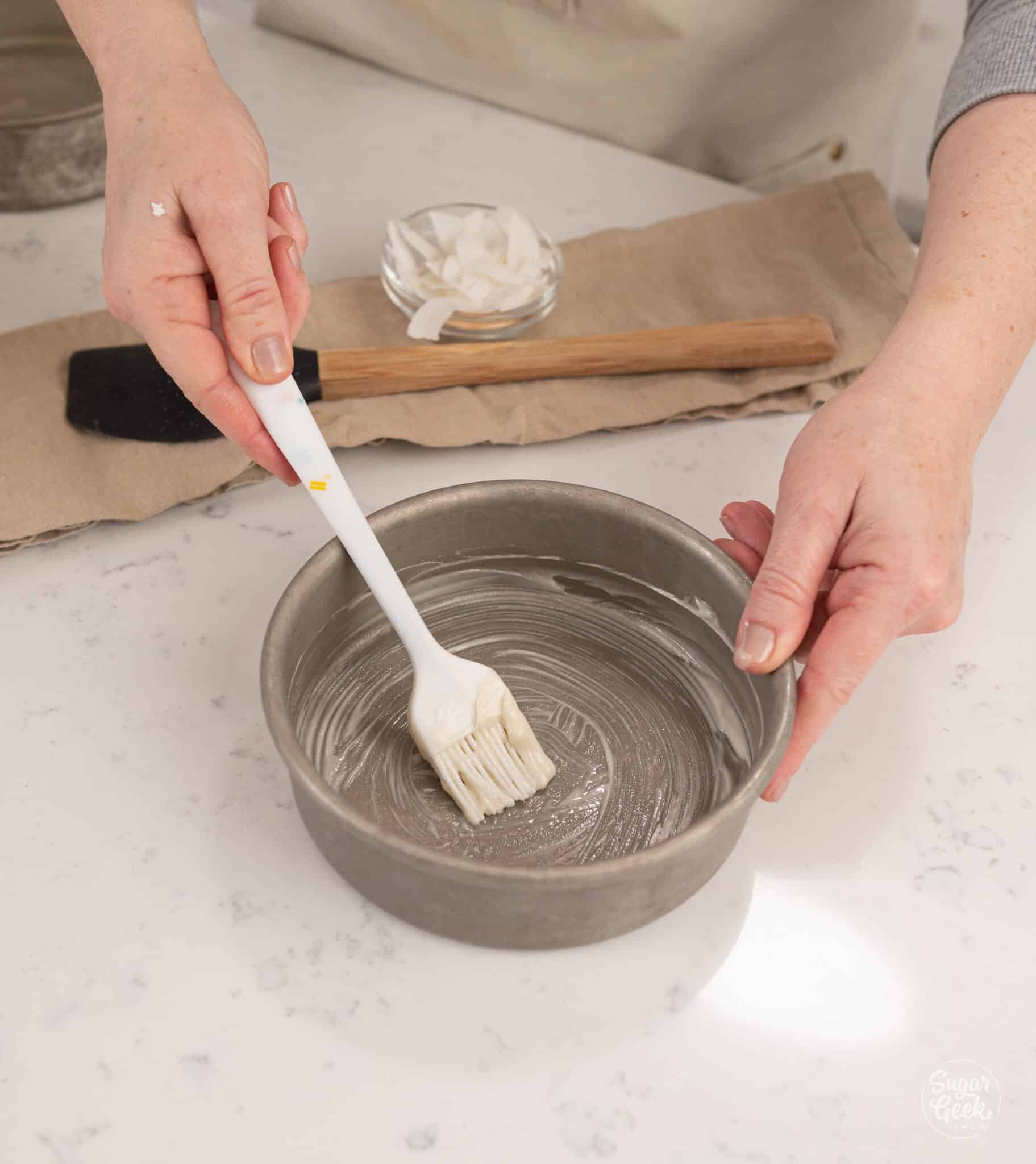 hands holding a pastry brush preparing a cake pan with pan release