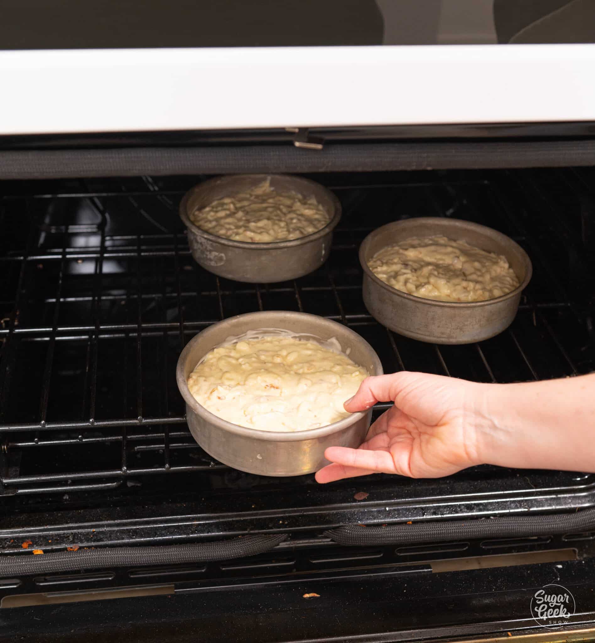 hand placing a cake pan with batter into an oven