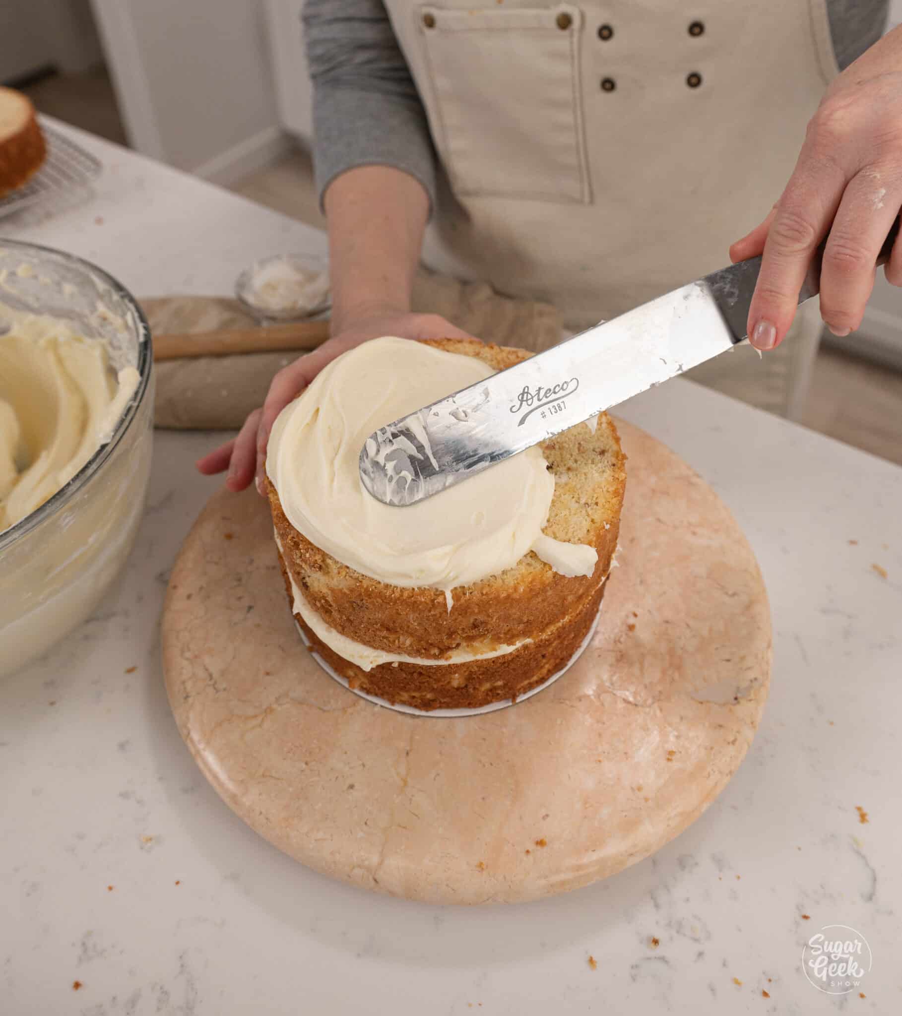 spreading cream cheese frosting on top of cake layer with an offset spatula