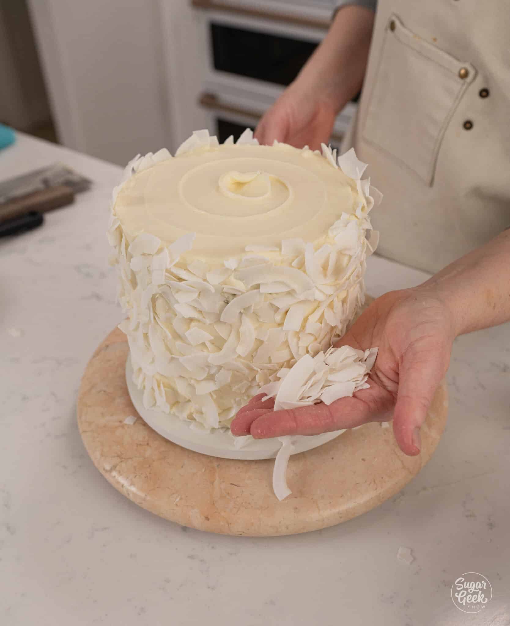 hand pressing coconut onto the side of a cake