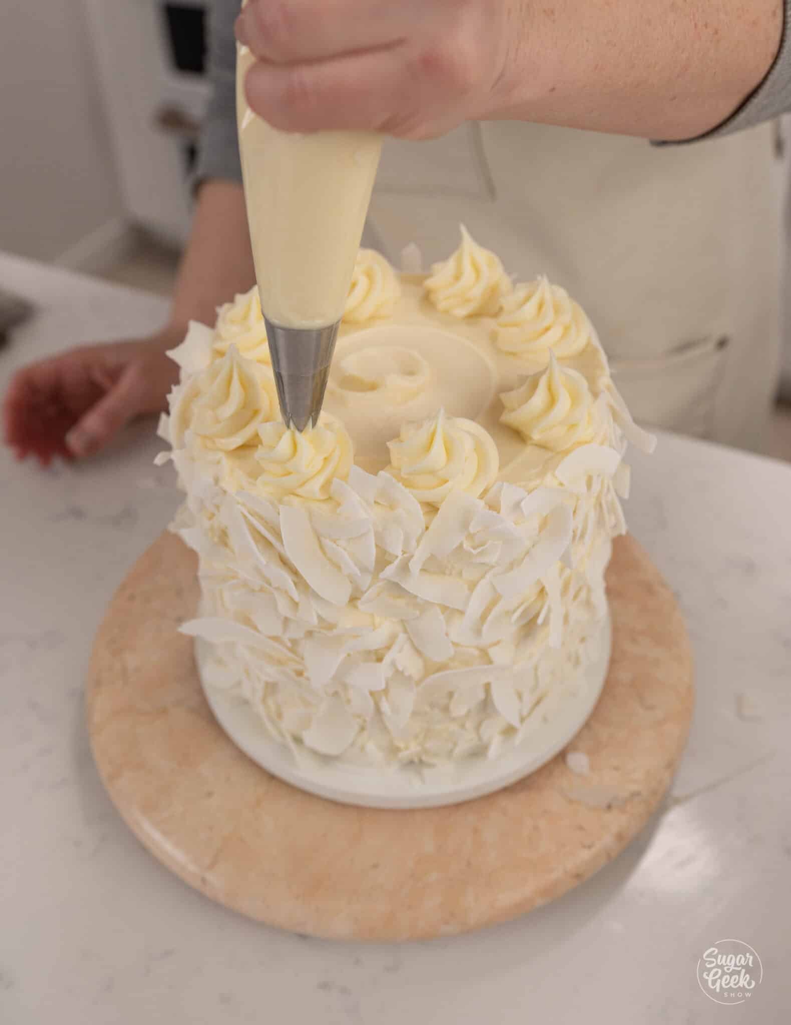hand piping swirls of frosting on top of a cake with a piping bag