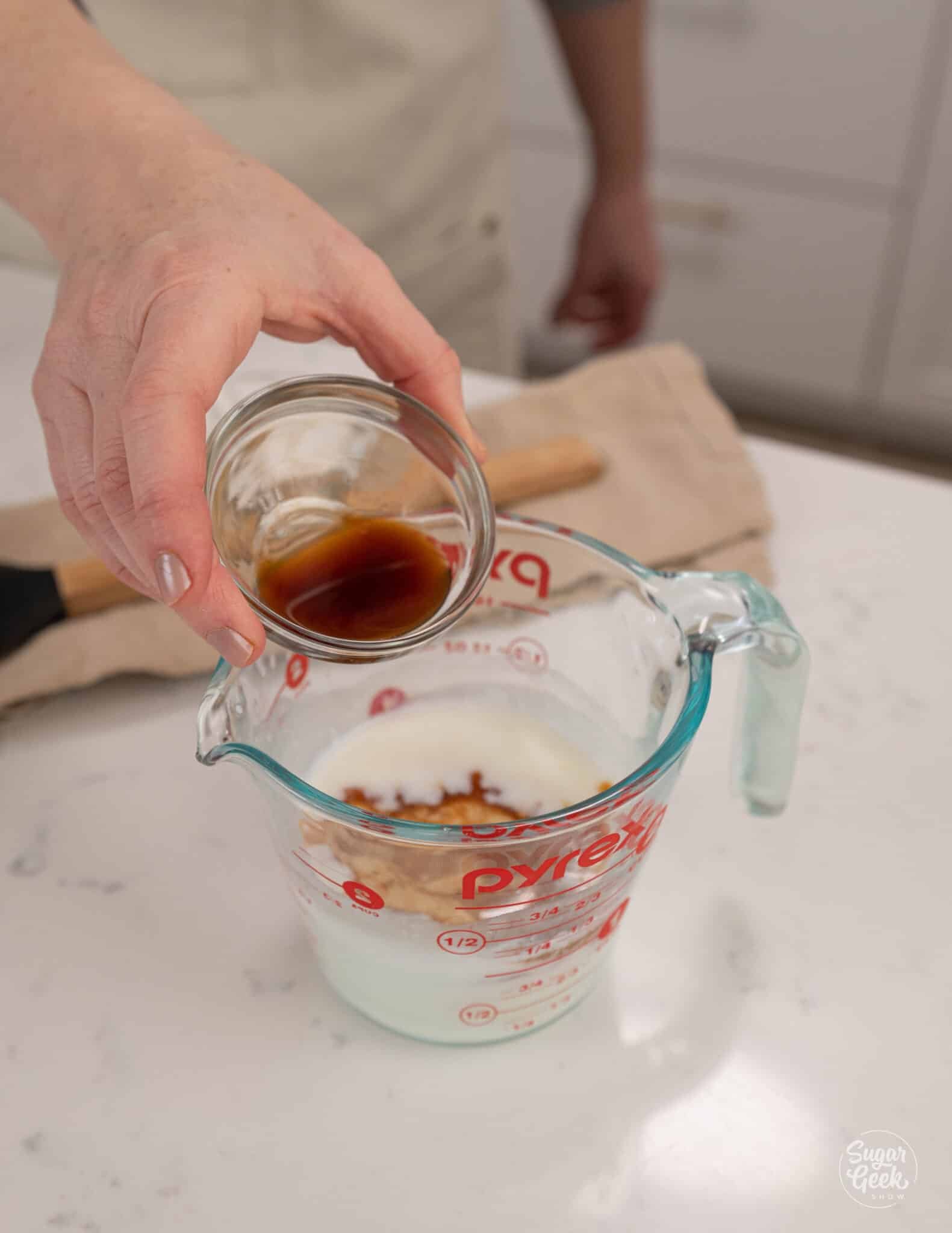 hand adding a bowl of vanilla to a measuring cup of buttermilk