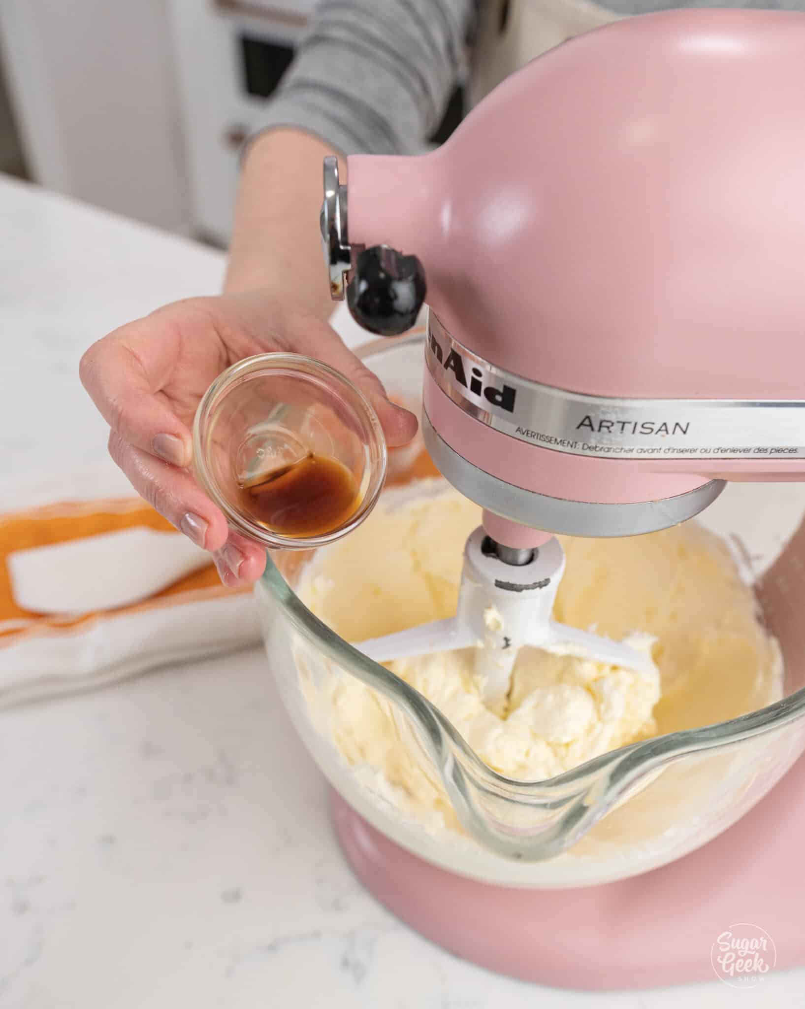 Hand pouring a container of sugar into a stand mixer bowl