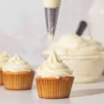 Piping cream cheese frosting onto a cupcake.