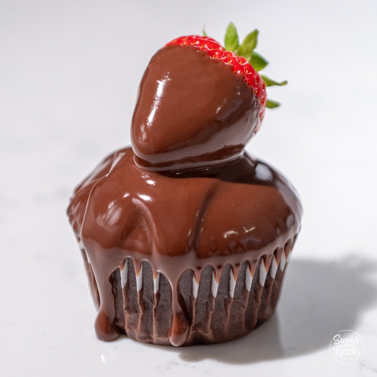 strawberry dipped in ganache on top of a chocolate cupcake