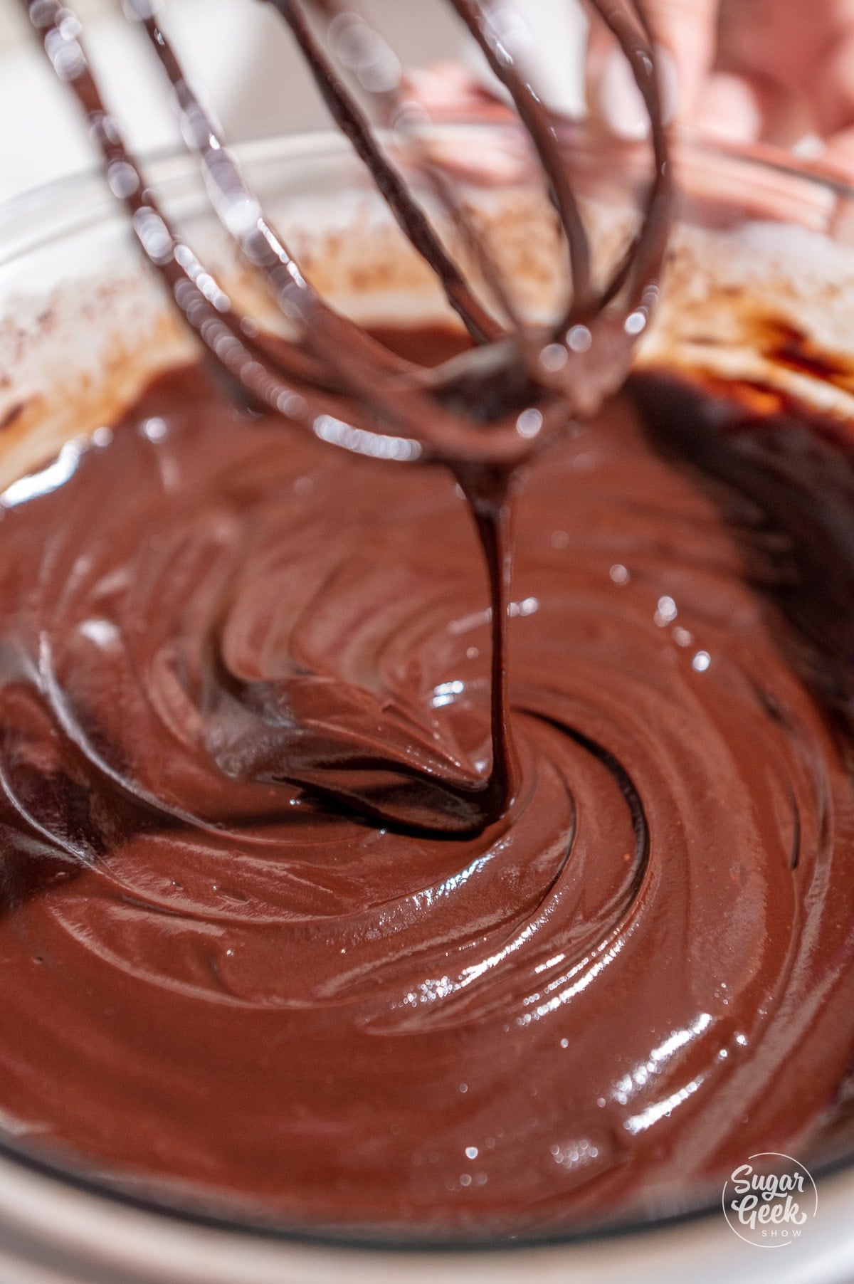 close up of whisked chocolate ganache drizzling off of a whisk