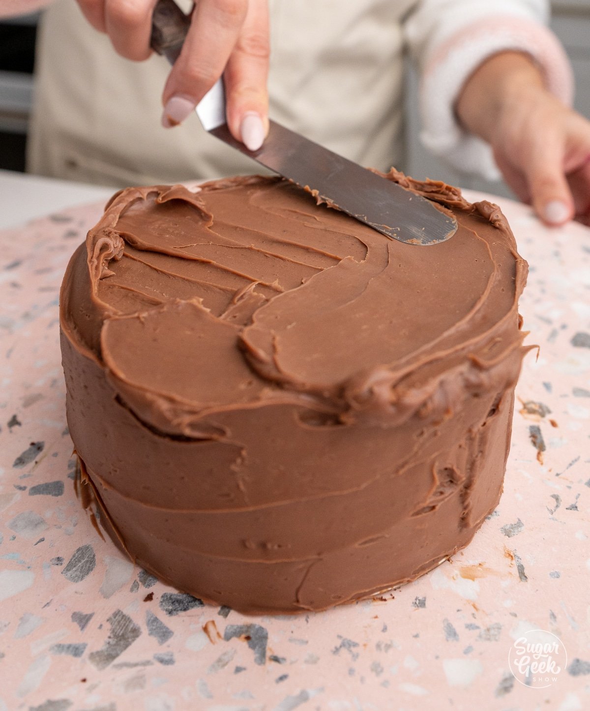 hand spreading chocolate ganache on the outside of a cake with a spatula