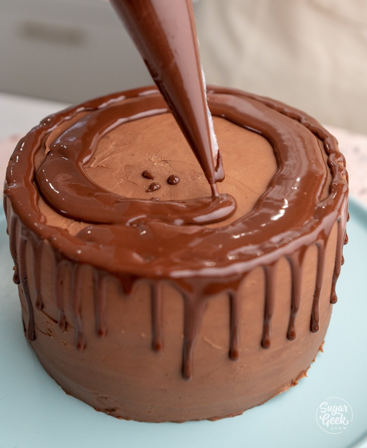 piping bag of ganache creating a drip on the sides and top of a cake
