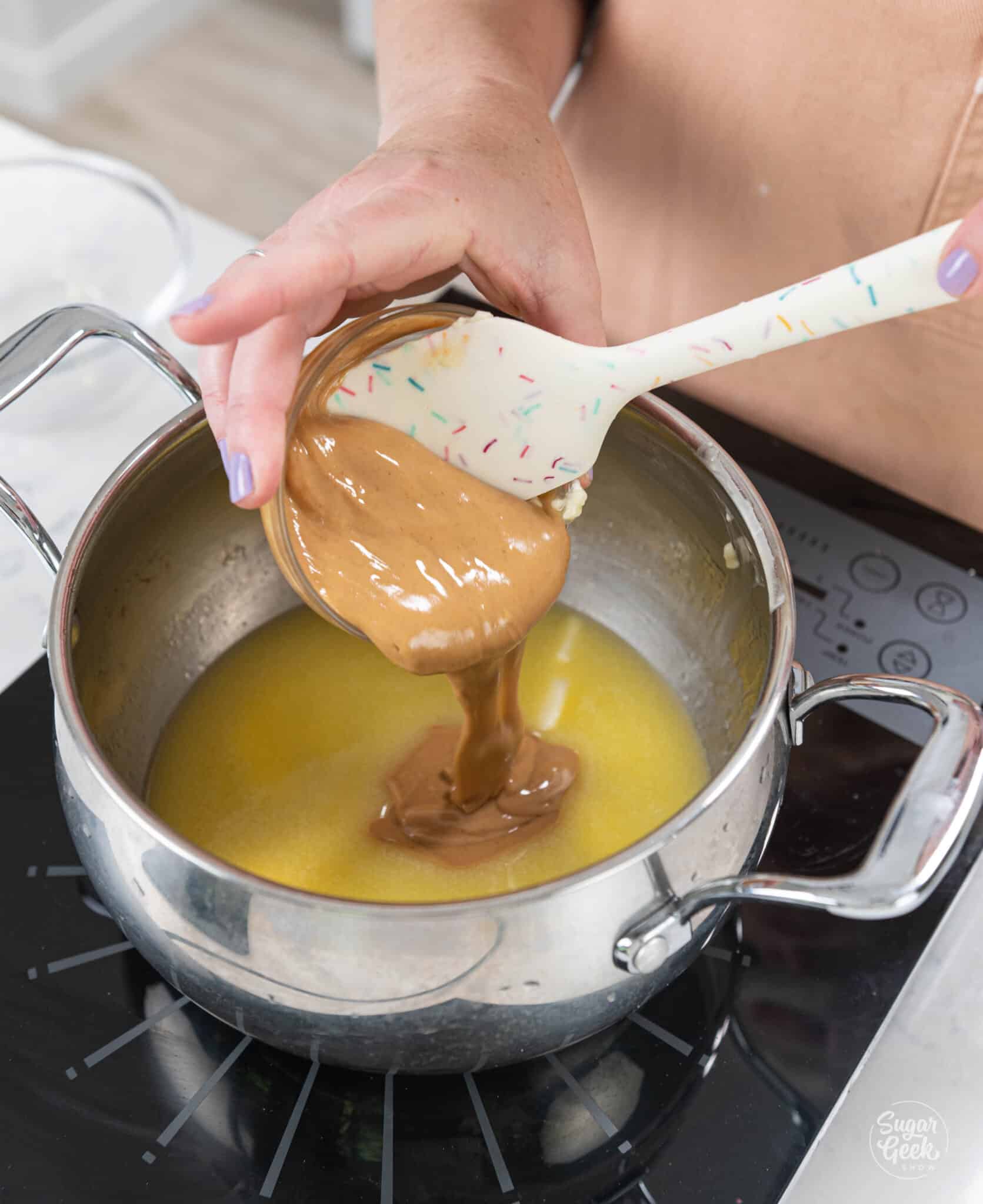 hand using spatula to scoop peanut butter into stove top.