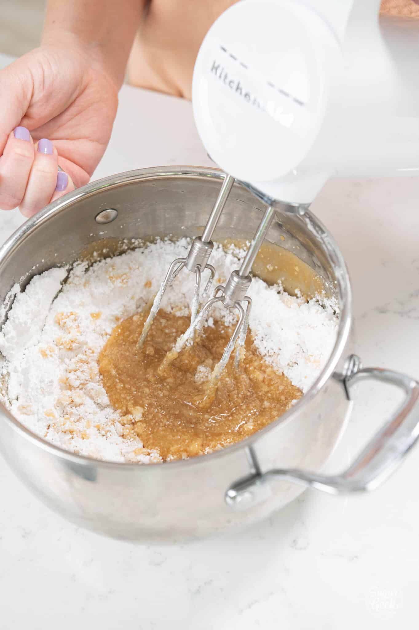 hand using hand mixer to whisk together powdered sugar and peanut butter glaze.