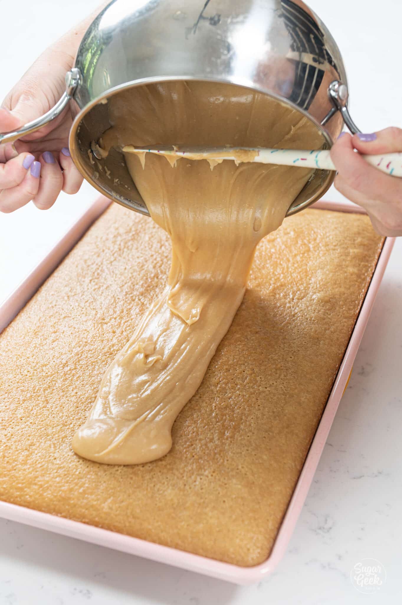 hand pouring bowl of peanut butter glaze onto baked sheet cake.