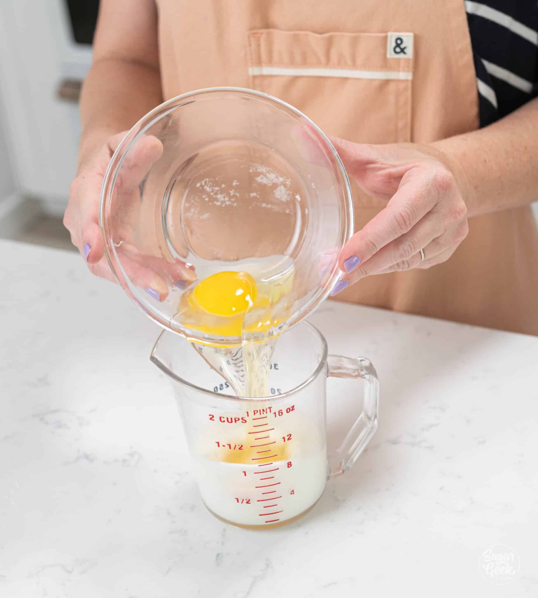 hands pouring bowl of eggs into measuring cup.