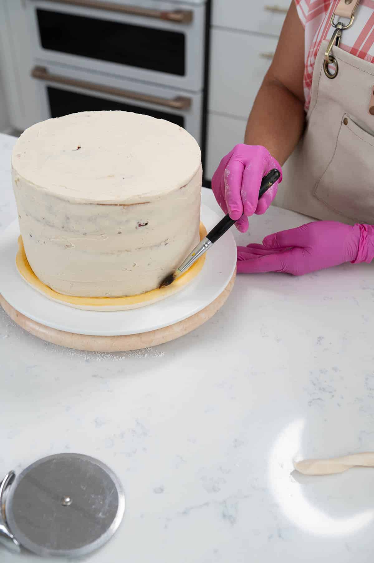 hand painting a strip of fondant on the outside of a cake