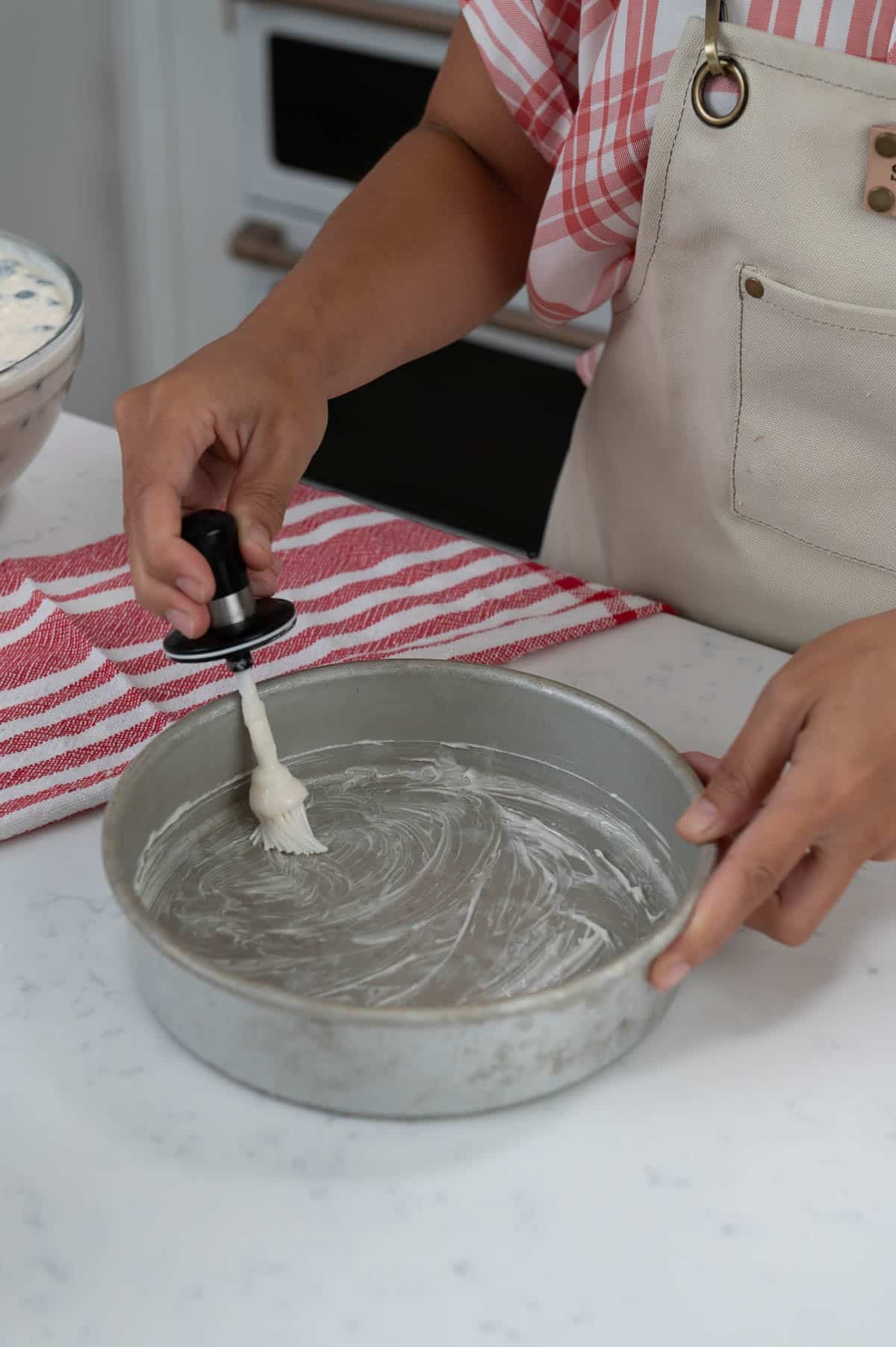 hand brushing a cake pan with cake goop