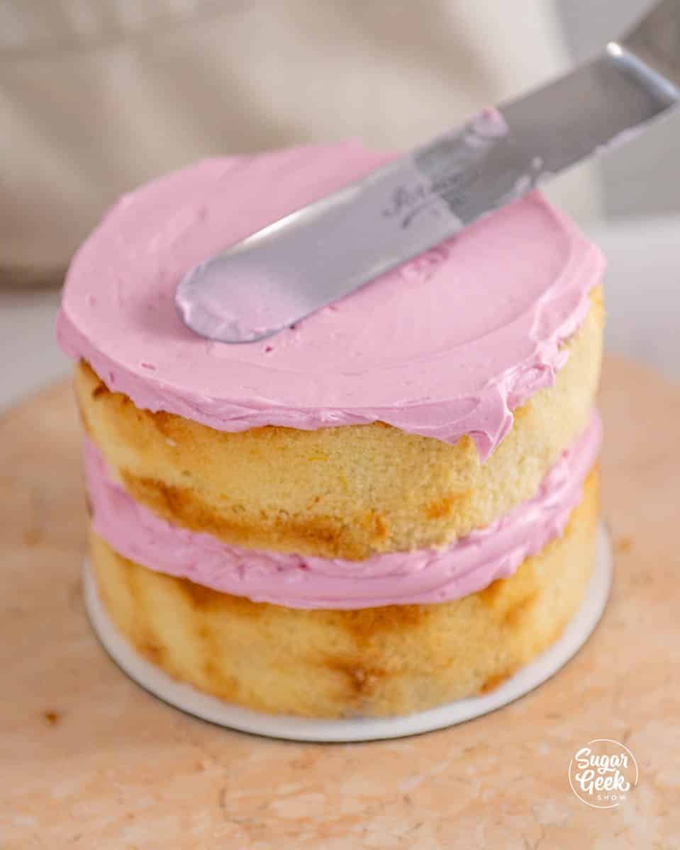 spreading pink buttercream on a cake