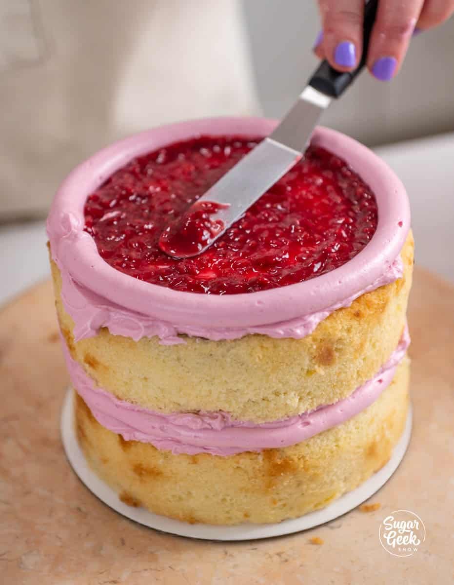 spreading raspberry filling in the center of a cake
