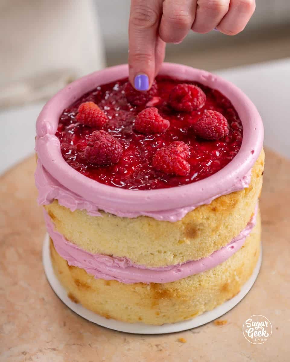 finger pressing raspberries onto a cake