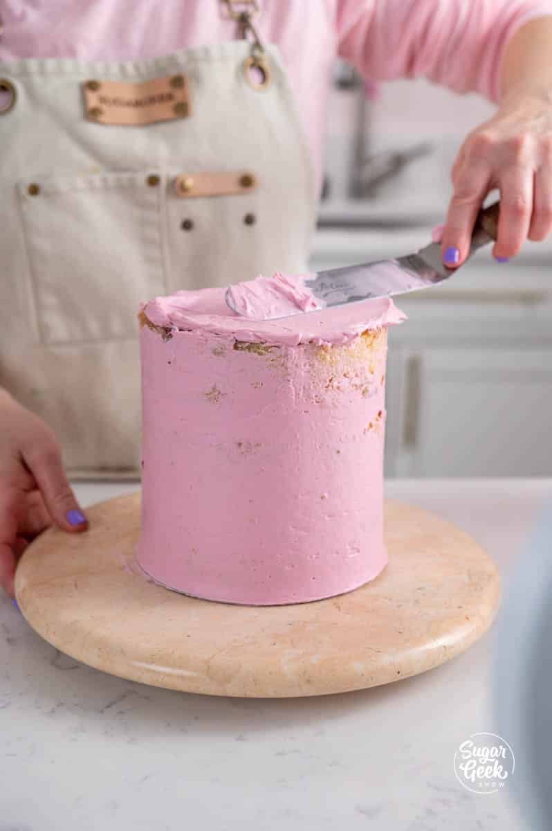 covering a lemon raspberry cake in pink frosting