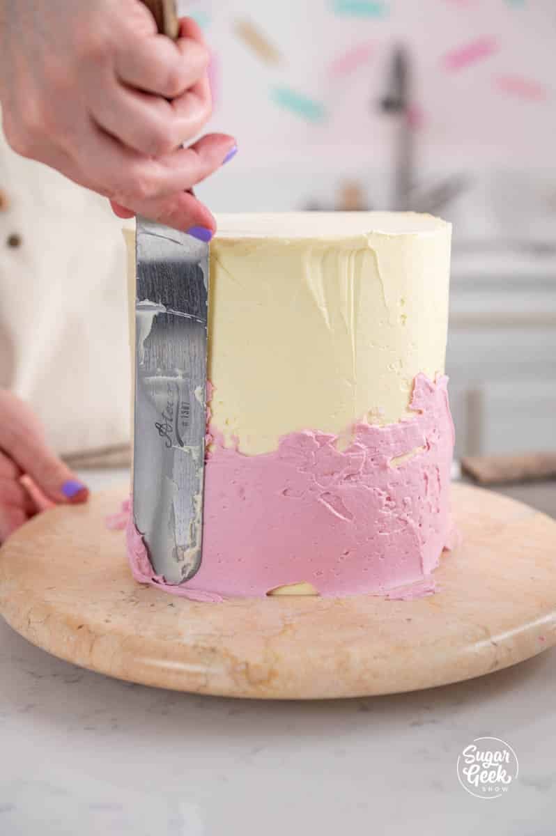 spreading pink buttercream onto the bottom of a cake