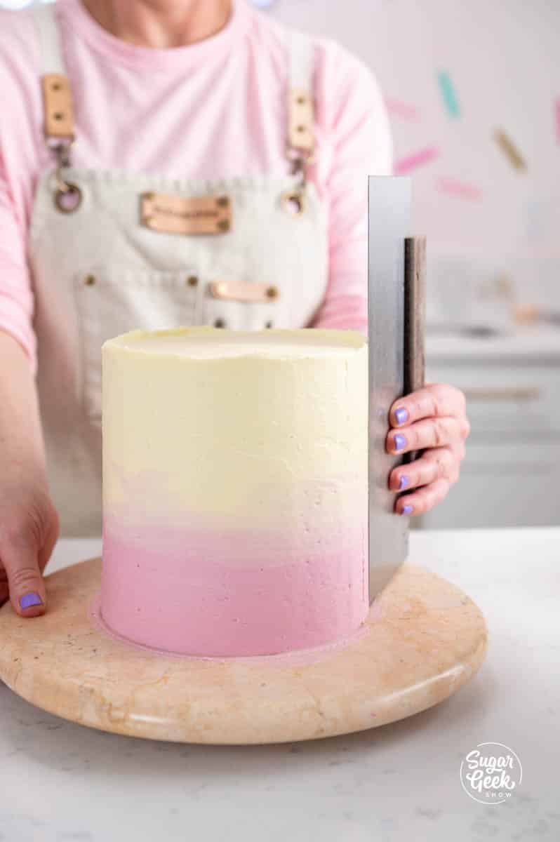 smoothing out a buttercream cake with a bench scraper