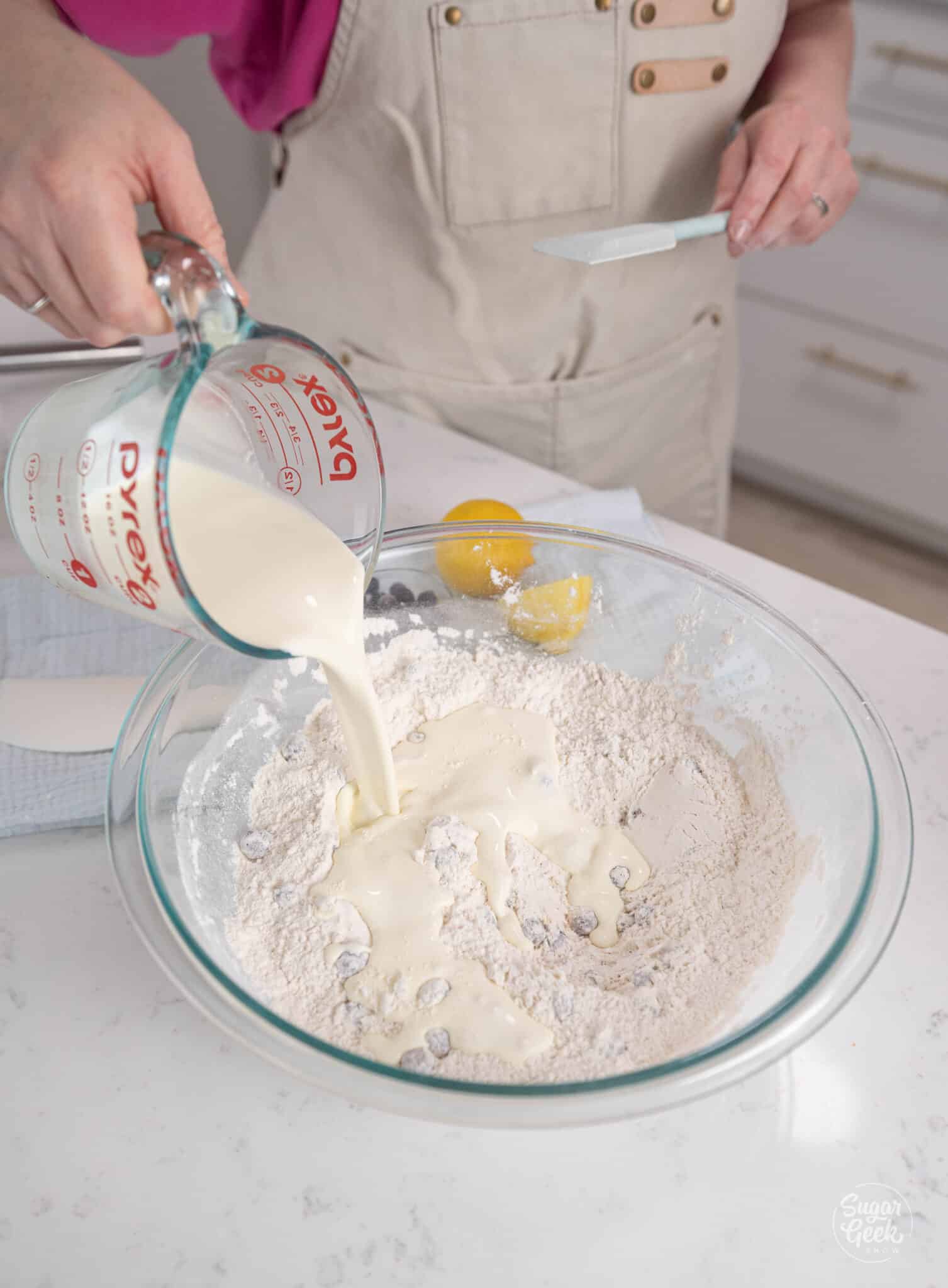 pouring cream from a container into a glass bowl of flour