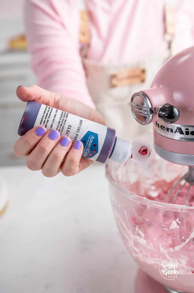 squeezing a bottle of food coloring into a stand mixer bowl