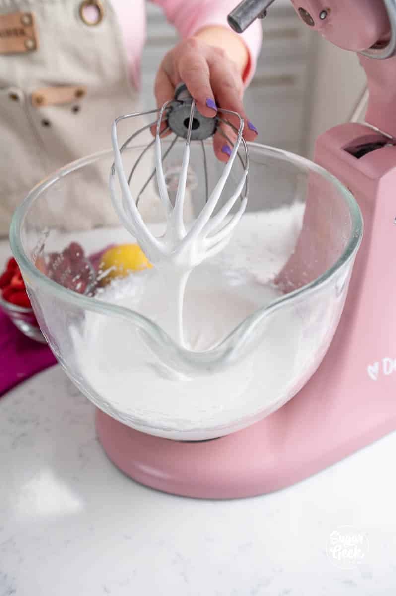 glossy mixed egg whites and powdered sugar in a stand mixer bowl