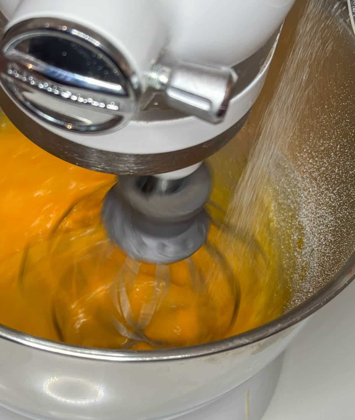 Close up of a mixer whisking eggs and sugar together.