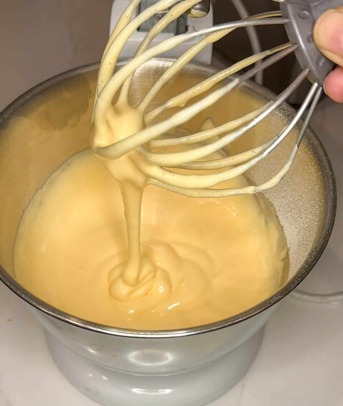 Thick and foamy eggs and sugar mixture dripping off a whisk attachment.