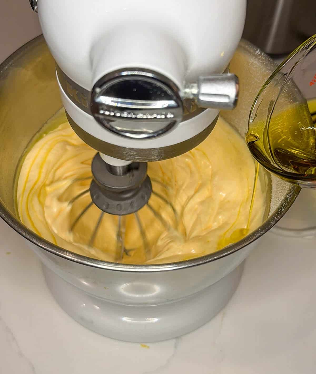 Olive oil being drizzled into whipping egg and sugar mixture.