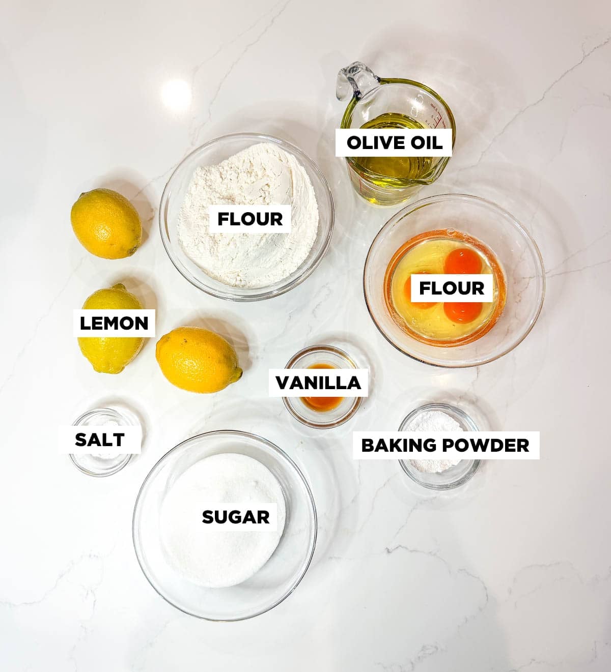 Lemon olive oil ingredients in bowls on a white countertop.