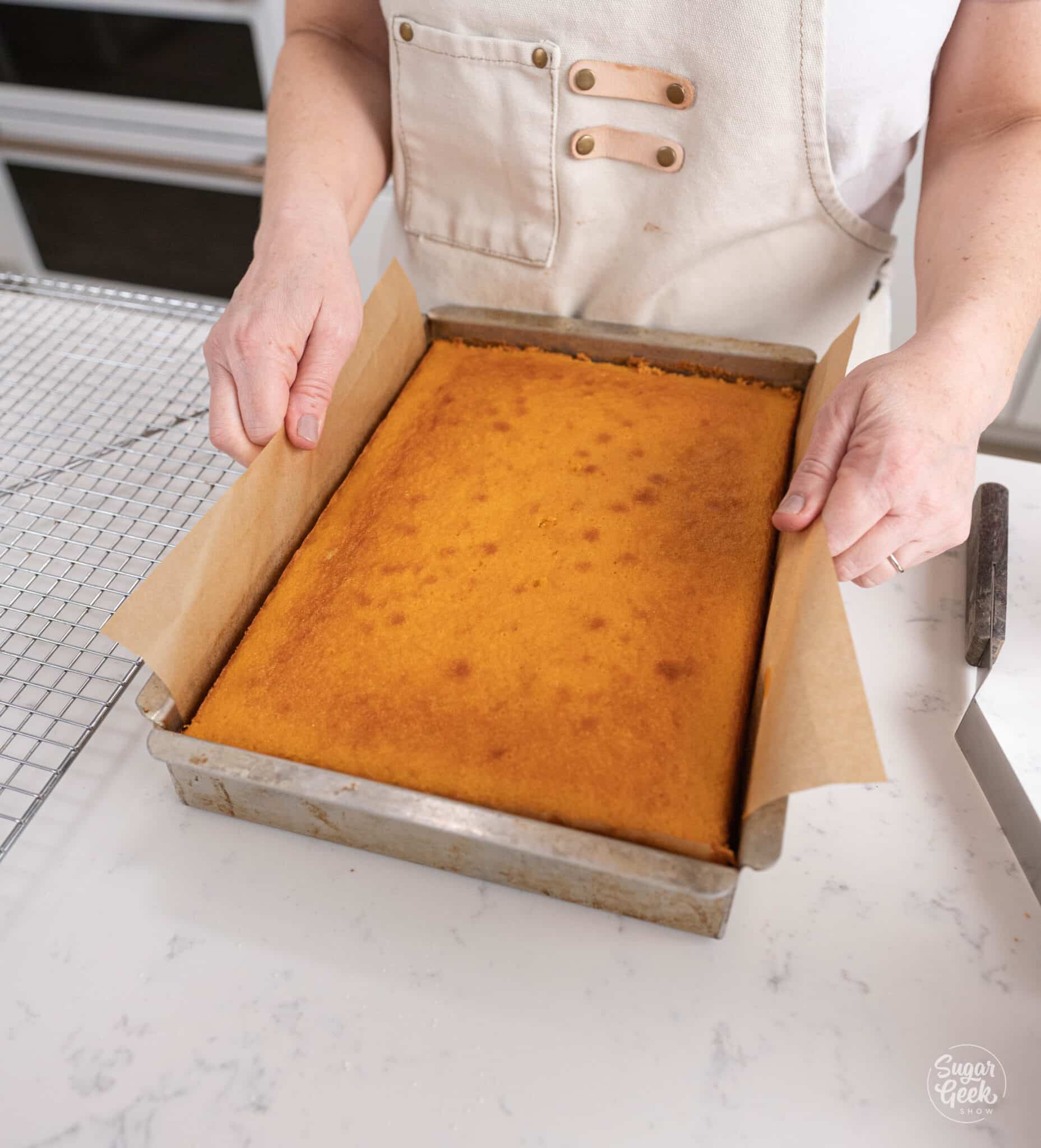 hands lifting a cake out of pan with parchment paper