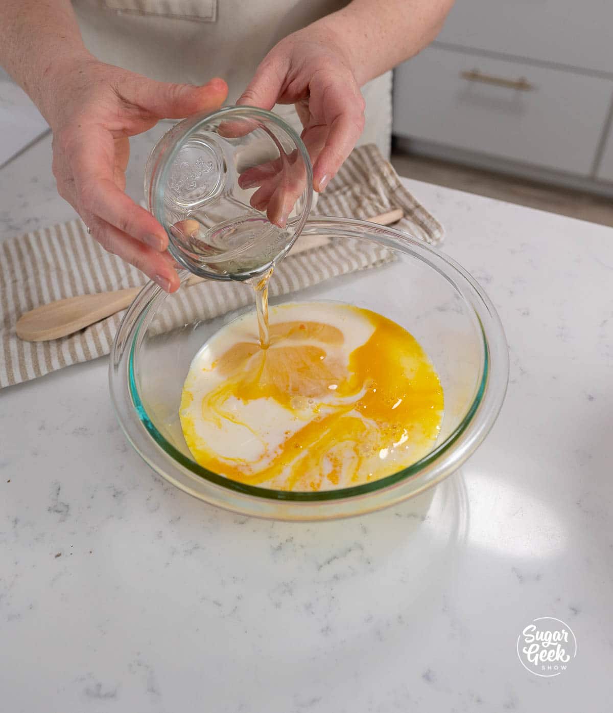 adding a bowl of oil to egg yolks and milk