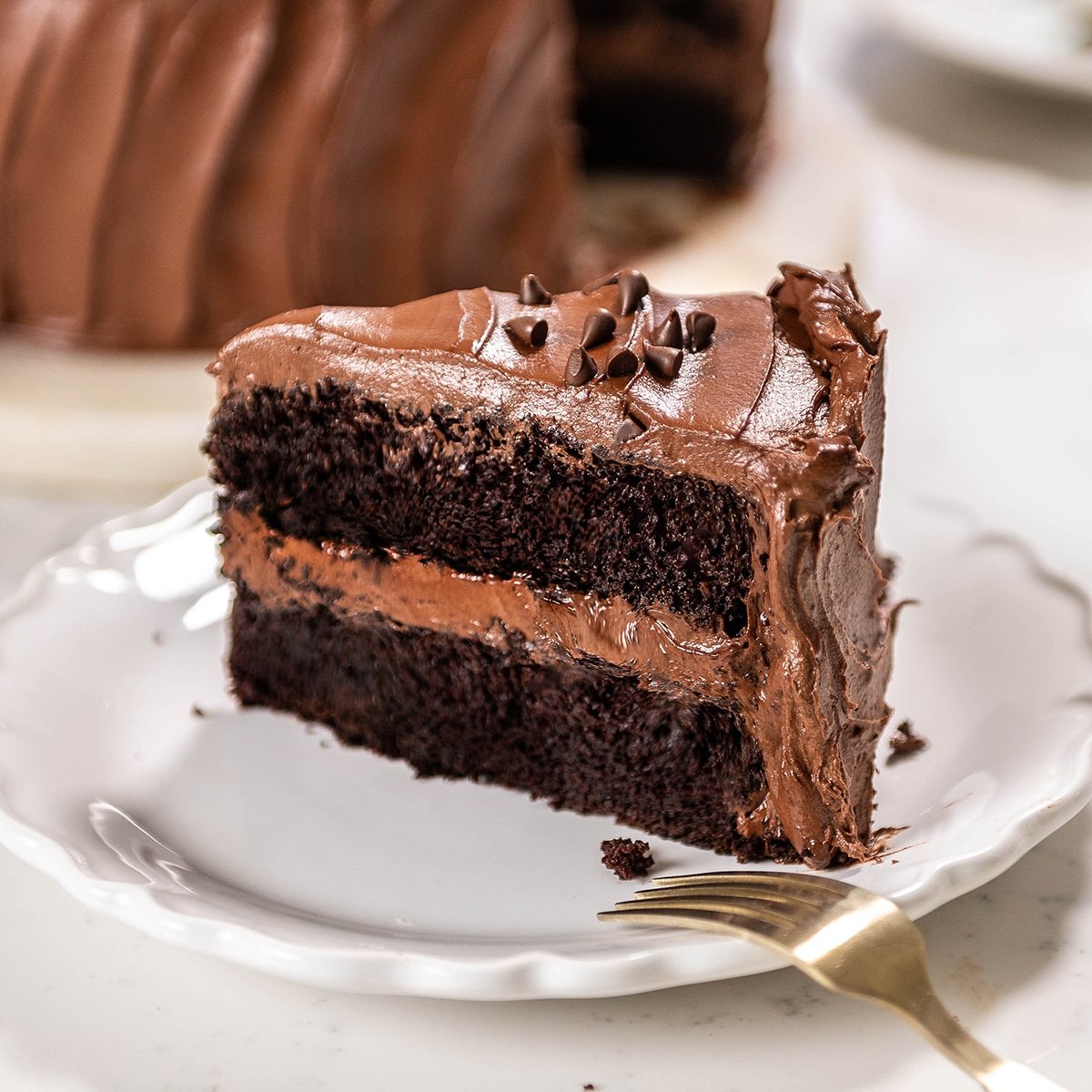 close up of a slice of chocolate cake with chocolate frosting on a. white plate